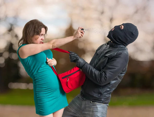 Zelfverdediging concept. Jonge vrouw is spuiten met pepperspray op dief. — Stockfoto