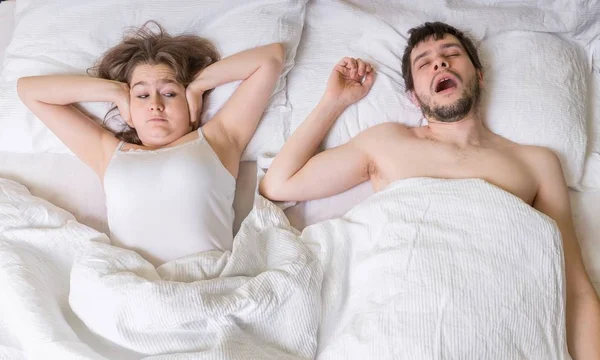 Conceito de ressonar. A jovem está a tapar os ouvidos. Homem está roncando na cama . — Fotografia de Stock