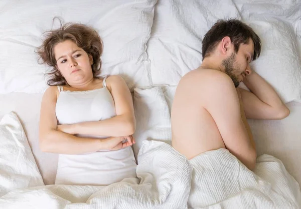 Impotence concept. Young man is sleeping in bed. Sad, disappointed and unsatisfied girlfriend lying near.