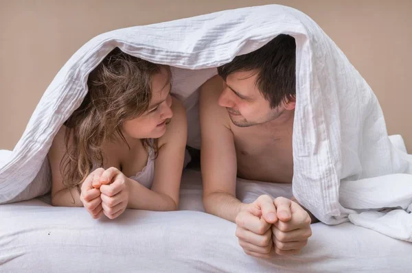 Jeune couple couché au lit sous la couverture et regardant dans leurs yeux — Photo