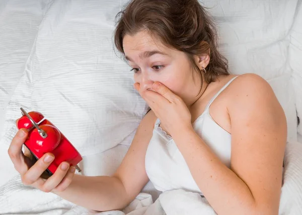 La jeune femme est choquée en regardant l'horloge. Elle est en retard et elle dort trop. . — Photo