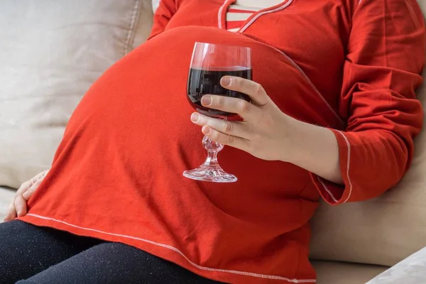 Drinking alcohol in pregnancy. Bad mother holds glass of wine in hand.
