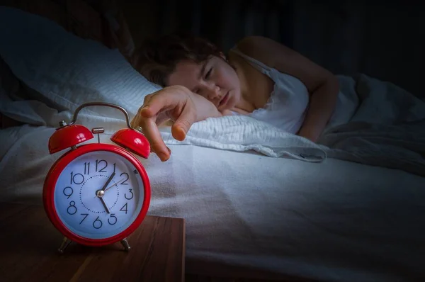 Mulher sonolenta jovem está acordando de manhã e está desligando o despertador . — Fotografia de Stock