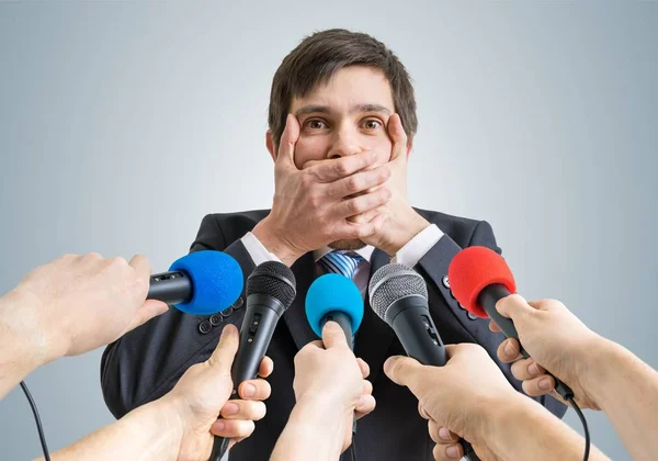 Funny politician is making no comment gesture. Many microphones in front. — Stock Photo, Image