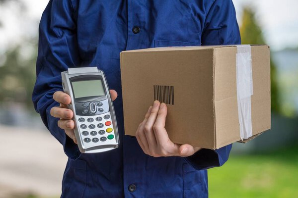 Package delivery concept. Man holds cardboard box and payment terminal in hands.