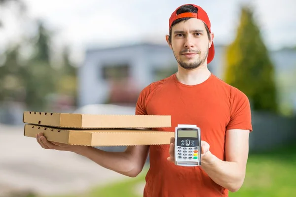 Young man is delivering pizza in boxes and holds payment terminal for paying with credit card.
