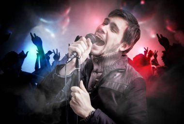 Genç adam bir somg disko kulüpte şarkı söylüyor. İnsanlar gece kulübünde dans ediyor.