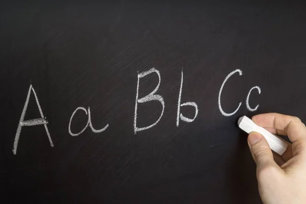 El profesor está escribiendo letra de alfabeto en pizarra con tiza. Educación en el concepto de escuela primaria . —  Fotos de Stock