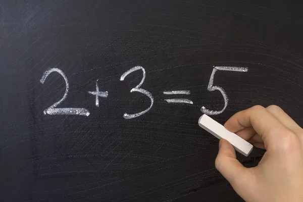 Guru menulis persamaan matematika sederhana pada papan tulis dengan kapur. Pendidikan dalam konsep sekolah dasar . — Stok Foto