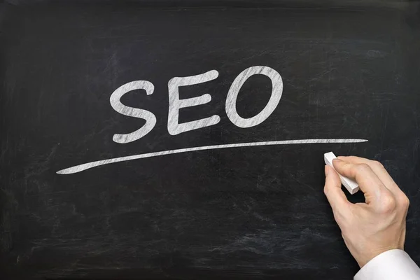 Hand is writing SEO (Search Engine Optimization) on blackboard. — Stock Photo, Image