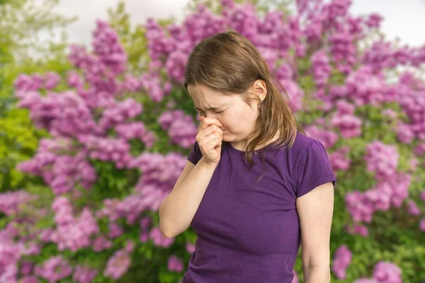 Pollen allergy concept. Young woman is sneezing. Flowering trees in background. — Stock Photo, Image