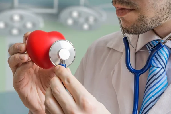 Кардиолог слушает красное сердце со стетоскопом . — стоковое фото