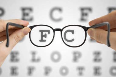 Hands holds black glasses in front of vision testing chart. Eye sight testing concept. clipart