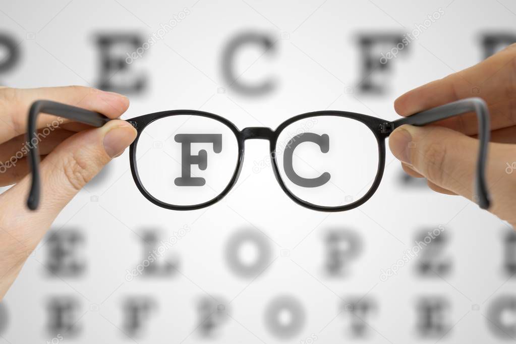 Hands holds black glasses in front of vision testing chart. Eye sight testing concept.