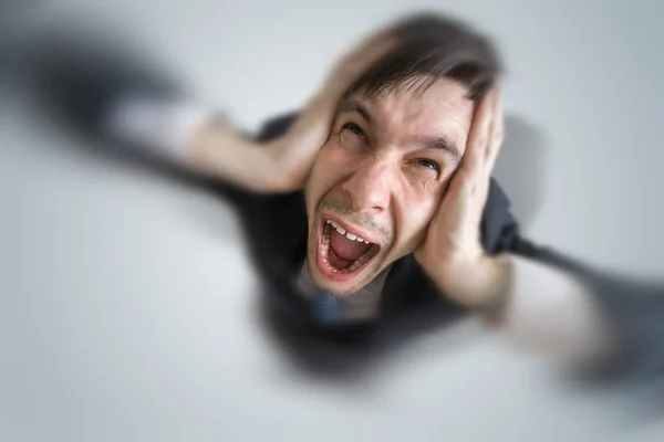 Junger schizophrener Mann leidet unter Kopfschmerzen und bedeckt seine Ohren mit Händen. — Stockfoto