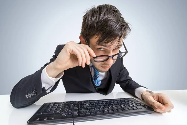 Homem suspeito de óculos está trabalhando com computador e olhando para você . — Fotografia de Stock