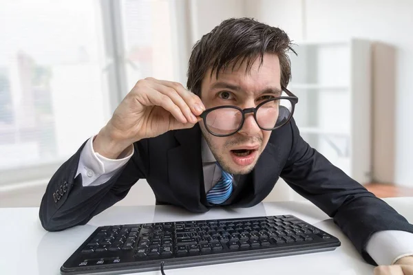 Confused or unsure man is working with computer and looking at you. — Stock Photo, Image