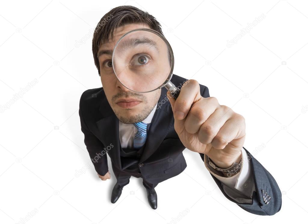 Young man is looking through magnifying glass. Isolated on white background. View from above.