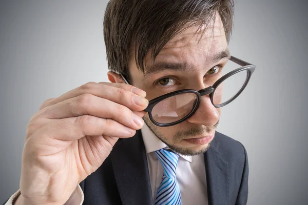 Young suspicious businessman is looking at you through glasses. — Stock Photo, Image