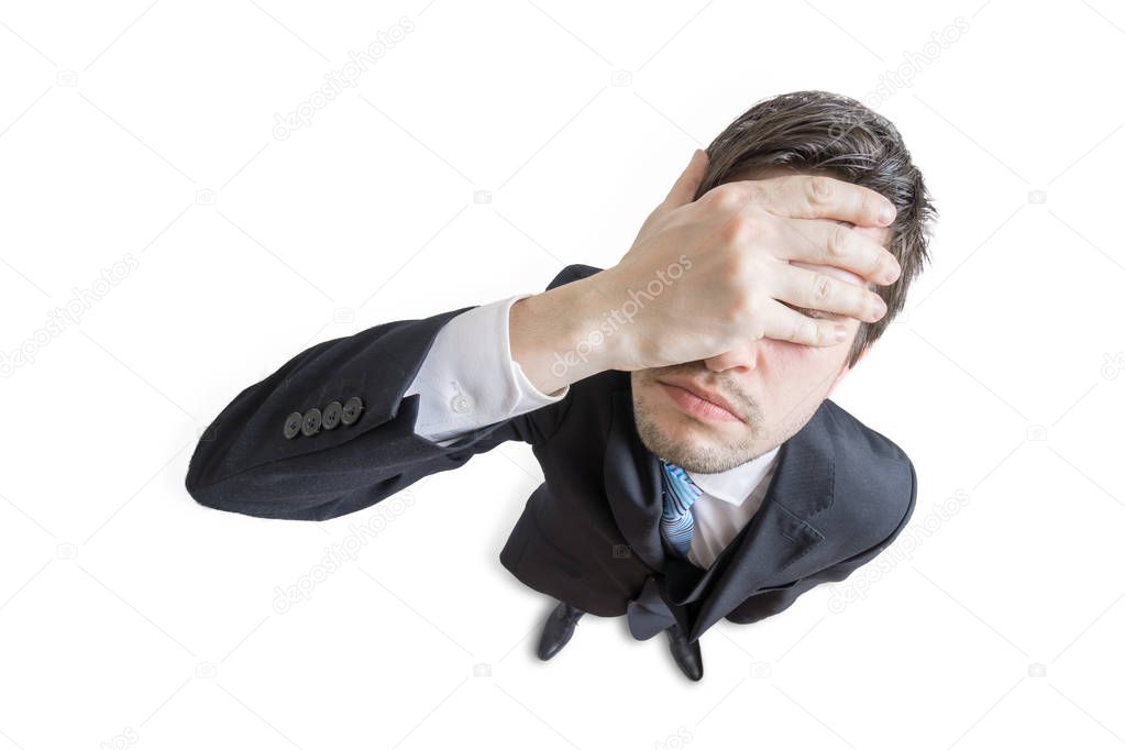 Young unhappy and stressed man made mistake and is covering his face with hand. Isolated on white background. View from top.