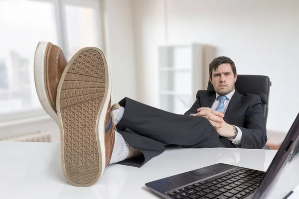 Молодой бизнесмен отдыхает на рабочем месте и стоит на ногах — стоковое фото