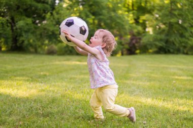 Küçük çocuk parkta futbol topuyla oynuyor.