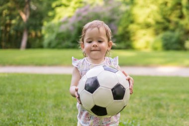 Küçük çocuk parkta futbol topuyla oynuyor.