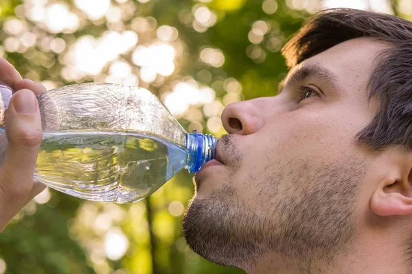Genç adam içme suyu şişe sıcak güneşli gün.