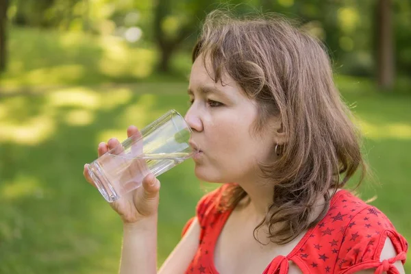 Giovane donna sta bevendo acqua dal vetro in natura a caldo soleggiato — Foto Stock