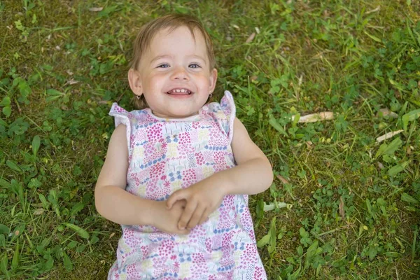 Niña feliz (un niño) está acostado sobre hierba verde en el parque . — Foto de Stock