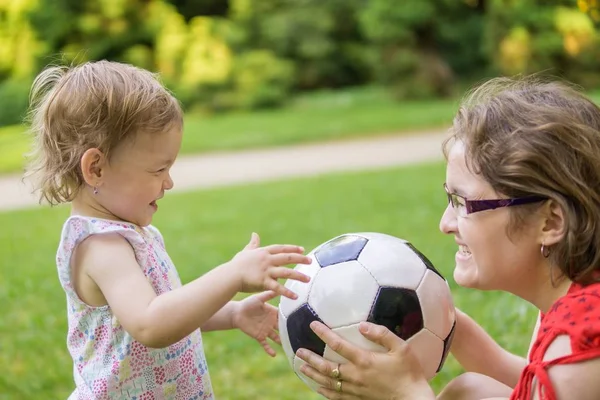 Madre y su hija están jugando con la pelota de fútbol en el parque . — Foto de Stock
