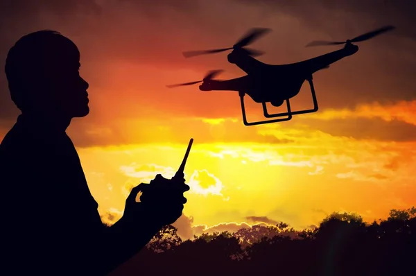 Silhouet van de mens die beheersing van een drone bij zonsondergang. — Stockfoto