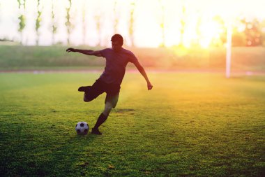 Futbolcu günbatımında stadyumda bir top ateş ediyor.