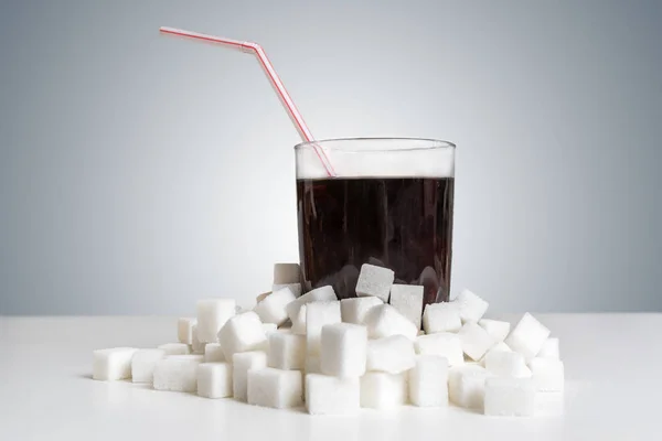 Bebida de cola em vidro e muitos cubos de açúcar ao redor. Comida pouco saudável — Fotografia de Stock