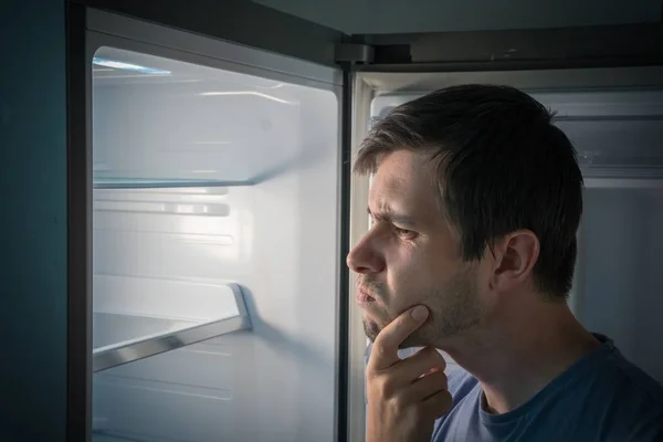 Hombre hambriento está buscando comida en la nevera vacía por la noche . — Foto de Stock