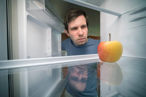Hungry man is looking for food in fridge. Only apple is inside e
