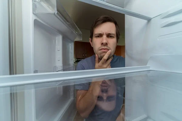 Głodny człowiek szuka jedzenia w pusta lodówka. — Zdjęcie stockowe