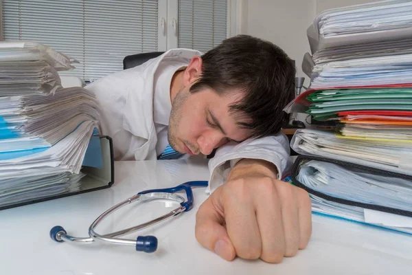 Trött och överarbetade läkare sover på skrivbord i office. — Stockfoto