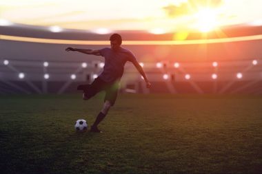 Soccer player is kicking a ball to the net in stadium at sunset. clipart
