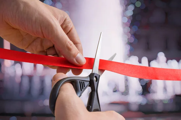 Man is cutting red tape or ribbon against defocused background. — Stock Photo, Image