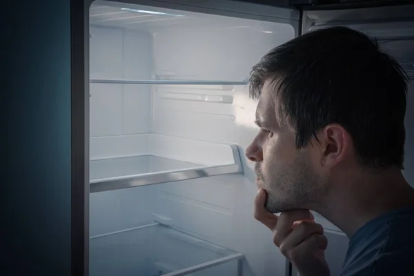 Homme affamé est à la recherche de nourriture à manger dans un réfrigérateur vide la nuit . — Photo