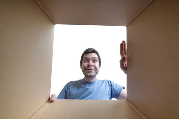 Jovem homem feliz está abrindo presente e olhando dentro da caixa de papelão — Fotografia de Stock