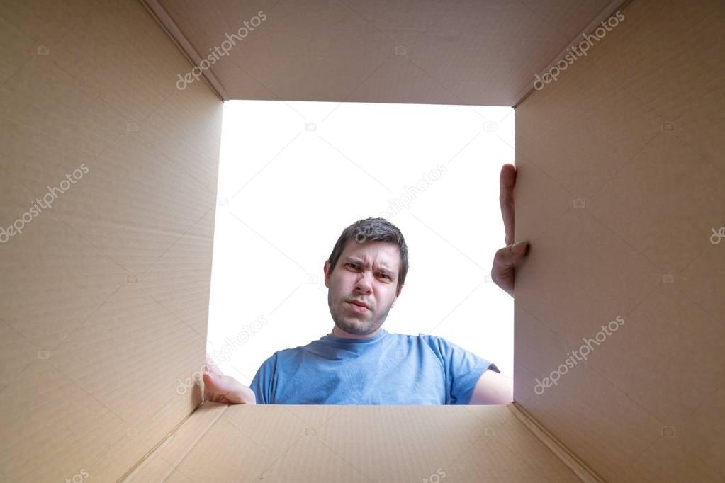 Young disappointed man is looking on gift inside cardboard box.