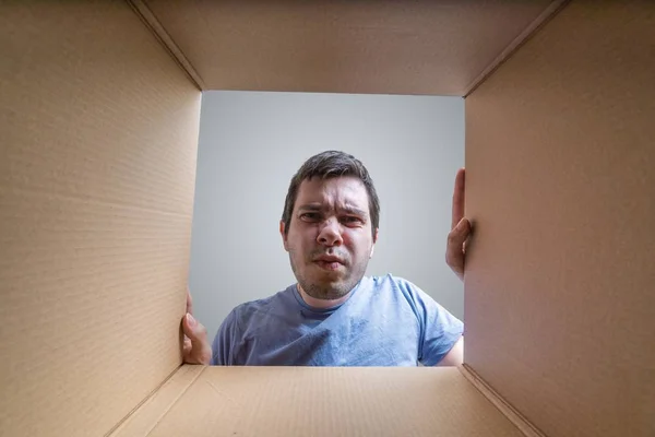 Молодой разочарованный человек смотрит на подарок внутри картонной коробки . — стоковое фото