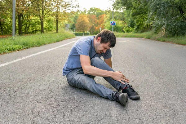 Yaralı adam bacağı kırıldı ve yolda oturuyor. — Stok fotoğraf