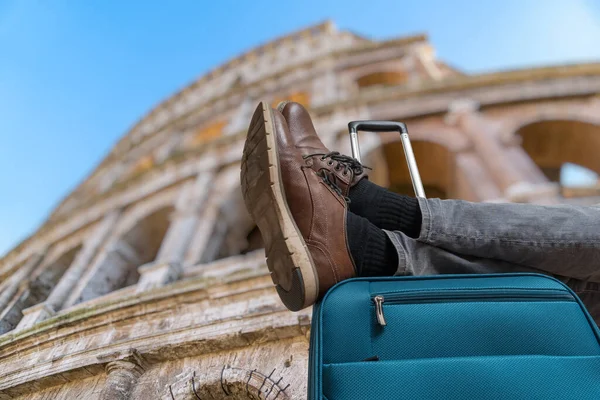 若い男はローマでリラックスしており スーツケースに足を持っています 背景にコロッセオ — ストック写真
