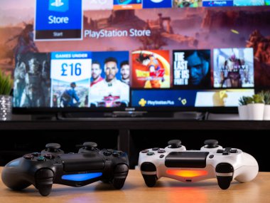 UK, Jan 2020: Pair of Sony Dualshock controllers white and black displayed in front of Playstation online store clipart