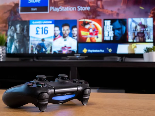 Reino Unido, Ene 2020: Sony Dualshock wireless controller with Playstation online store on television screen — Foto de Stock