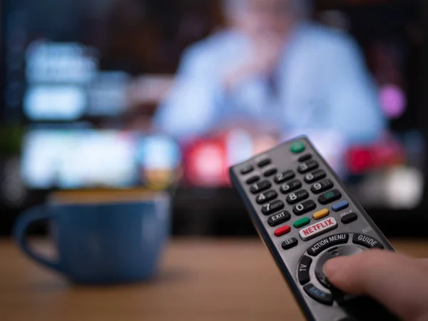 Uk, January 2020: close up of Tv remote with TV behind showing Netflix menu — 图库照片