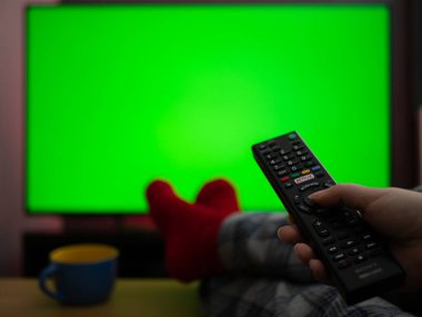 Pijamalarını giyip ayaklarının üzerinde oturmuş yeşil ekran krom tuşlu televizyon izliyorsun.